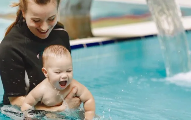 Маленький ребёнок учится плавать под руководством инструктора