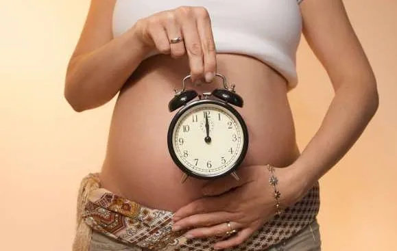 Будильник на фоне живота беременной девушки
