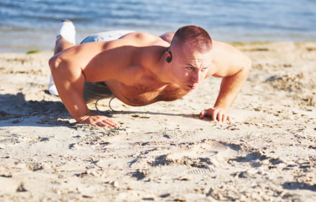 Мужчины выполняет спортивные отжимания на песчаном берегу реки