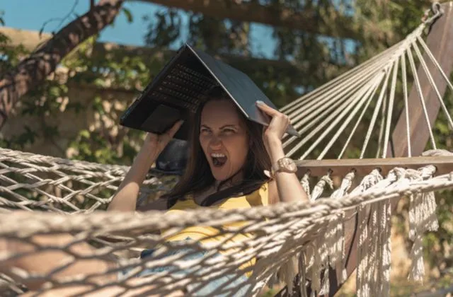 Женщина в гамаке с ноутбуком над головой, летняя жара