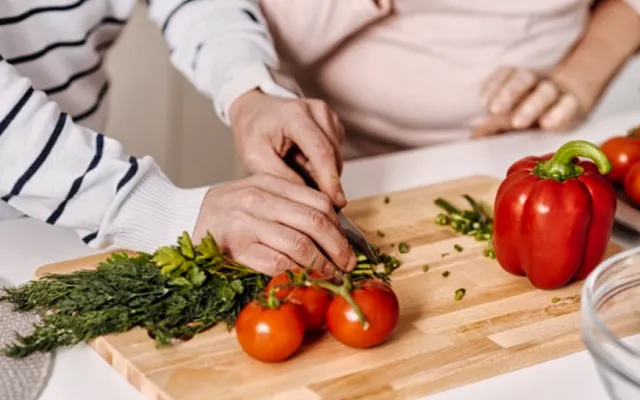 Пара пожилых людей готовит диетический салат из зелени и томатов