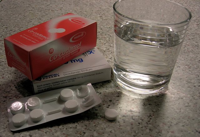 Упаковка болеутоляющих лекарственных средств рядом со стаканом воды